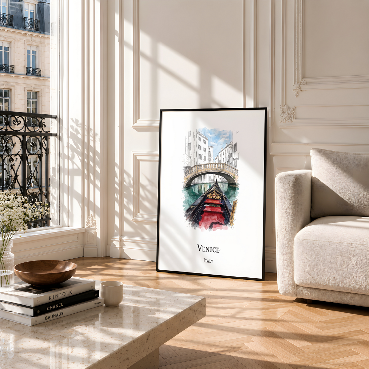 A framed watercolour art print of Venice, Italy, leaning against a wall in a bright, modern living room with a beige sofa and wooden floors.