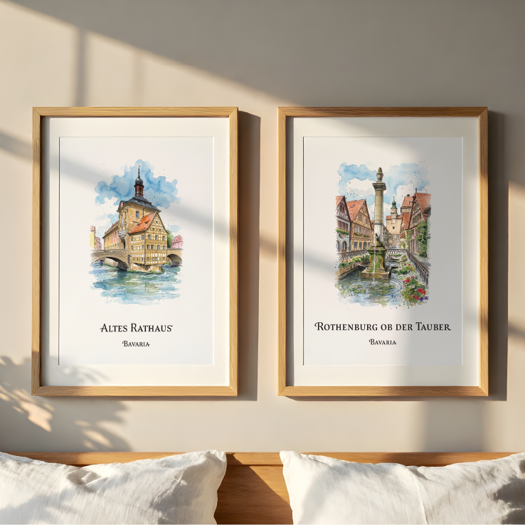 Two framed watercolour art prints hang on a beige wall above a wooden headboard. The left print shows 'Altes Rathaus' both in Bavaria, with the Town hall illustration, and the right print shows 'Rothenburg ob der Tauber' with a fountain and canal scene.