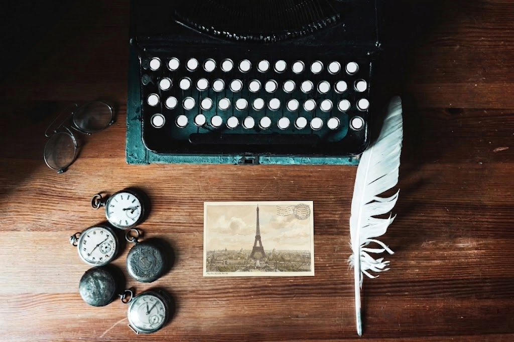 Vintage typewriter, pocket watches, feather quill, and postcard on a wooden surface