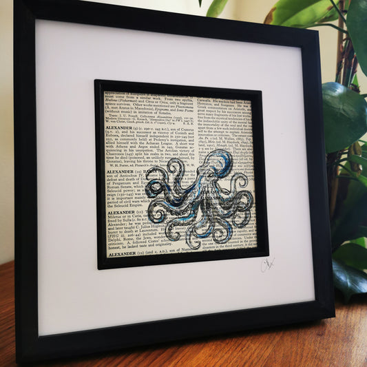 A framed and mounted artwork of a blue watercolour and ink illustration of a Kraken Octopus on a vintage dictionary page.