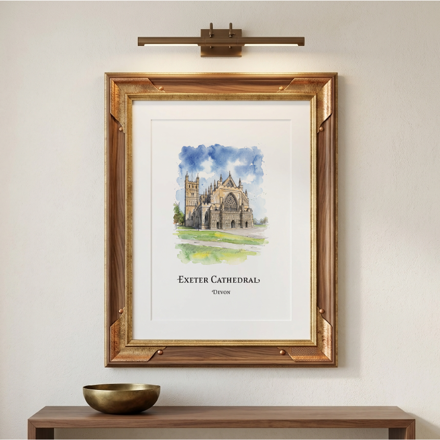 A framed art print of Exeter Cathedral, featuring a watercolour painting of the cathedral under a blue sky, displayed on a beige wall above a wooden console table with a gold bowl. A brass wall sconce is mounted above the frame.