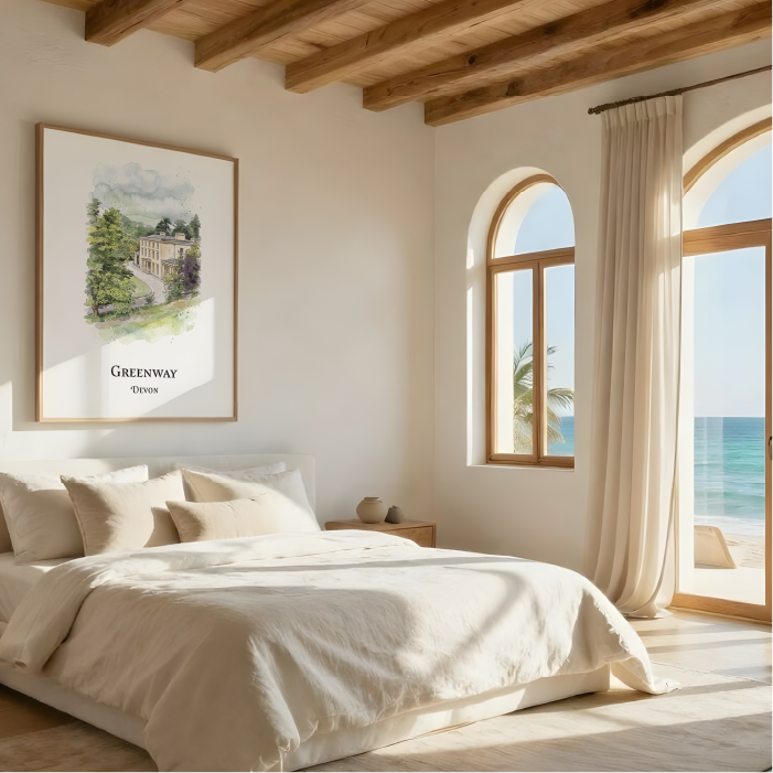A framed art print featuring a watercolour landscape of Agatha Christie's House, Greenway, Devon. styled on a warm off-white bedroom wall above a bed with neutral linens. The room has a rustic aesthetic with exposed wooden ceiling beams, a wooden nightstand, and large arched windows looking out to the ocean.