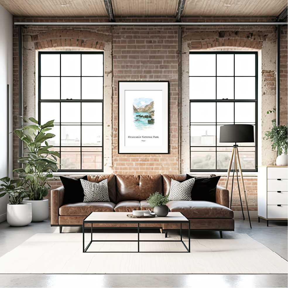 A styled living room interior with a brown leather sofa, black accent pillows, a black coffee table, brick walls, large industrial windows, potted plants, and a framed print of Huascarán National Park hanging above the sofa.