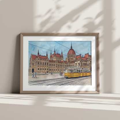 A framed art print depicting the Budapest City Hall and a yellow tram, styled on a shelf against a wall with soft leaf shadows.