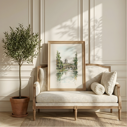 A framed landscape watercolour print of Castle Howard, Yorkshire, leaning against a cream upholstered wooden chaise lounge in a sunlit room, with a potted olive tree on the left and decorative pillows on the sofa.