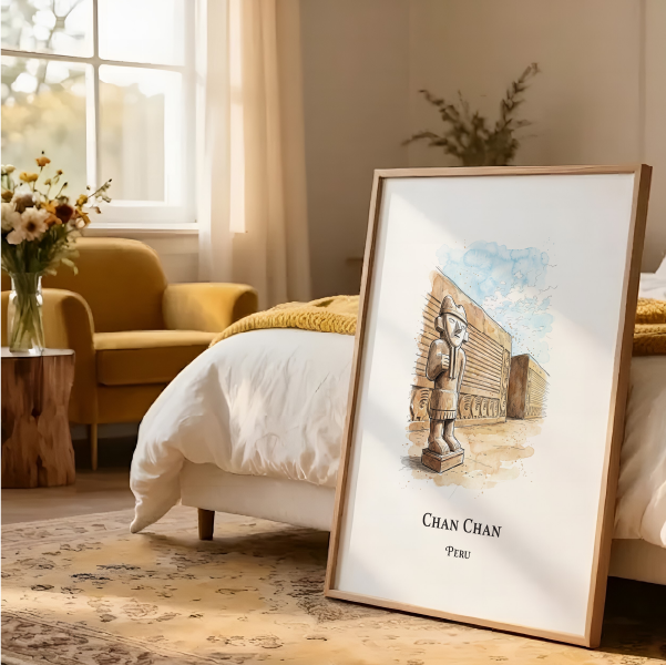 A framed art print featuring a watercolour illustration of a statue and the text 'CHAN CHAN PERU' is propped up on a bed in a warm, modern bedroom setting.