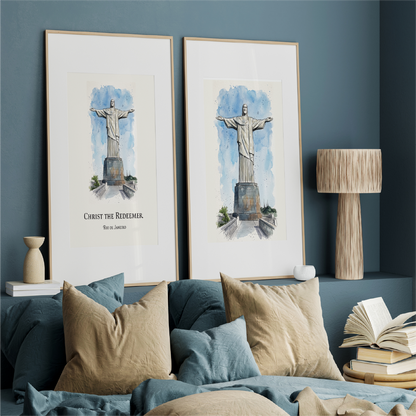 Two framed watercolour prints of Christ the Redeemer hanging on a blue wall above a bed with beige and blue pillows. The prints are shown in a styled bedroom setting.