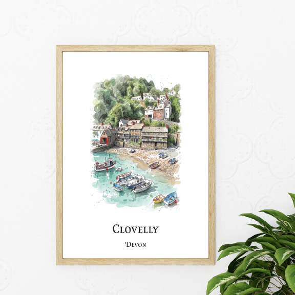 A framed watercolour art print of Clovelly, Devon, featuring a coastal harbour scene with boats and buildings, displayed on a white wall next to a green houseplant.