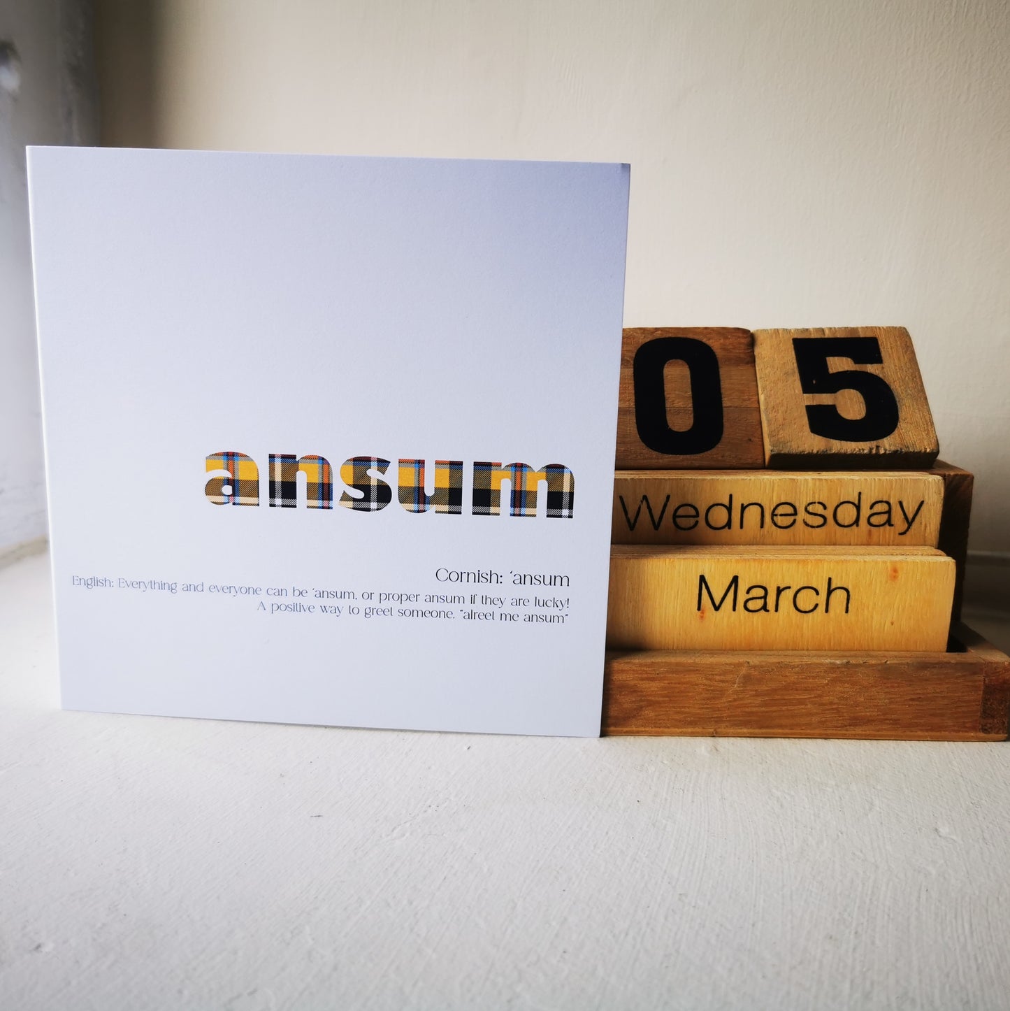 Wooden blocks with '05 Wednesday March' and a card with 'ansum' on a white surface.