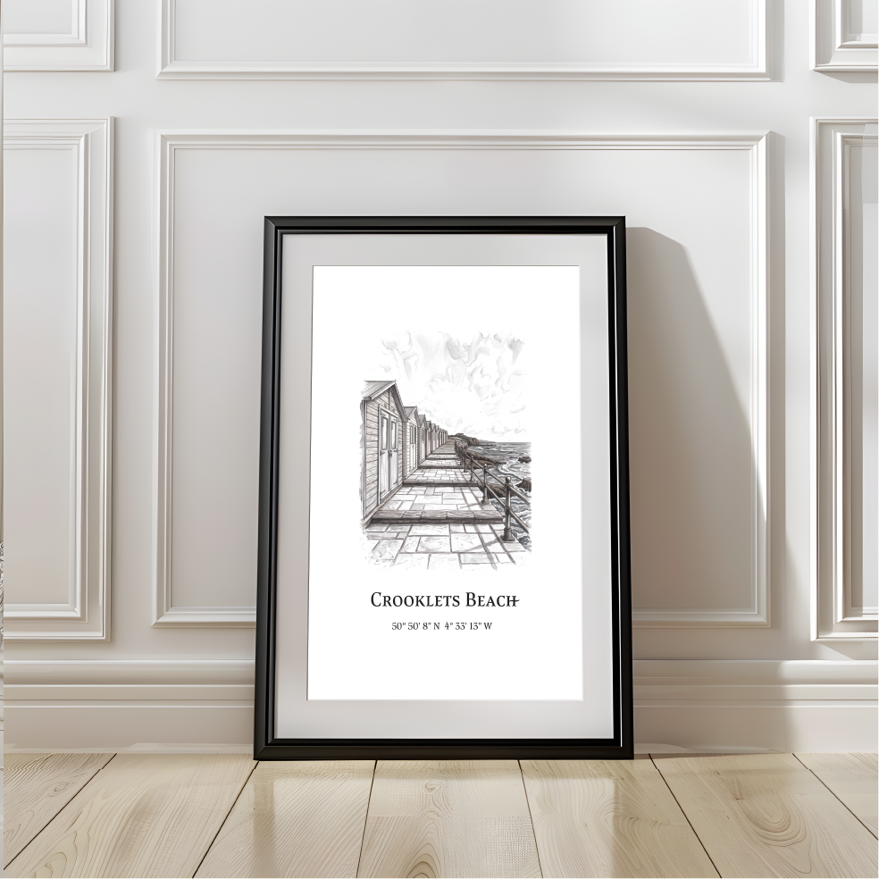 A framed black and white sketch poster of Crooklets Beach, displayed leaning against a white paneled wall on a light wood floor.