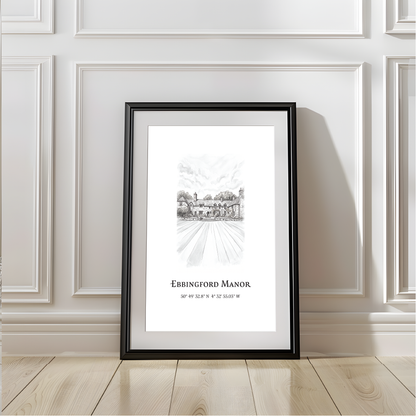 A framed black and white architectural art print of Ebbingford Manor in Budel, leaning against a white paneled wall on a light wood floor.