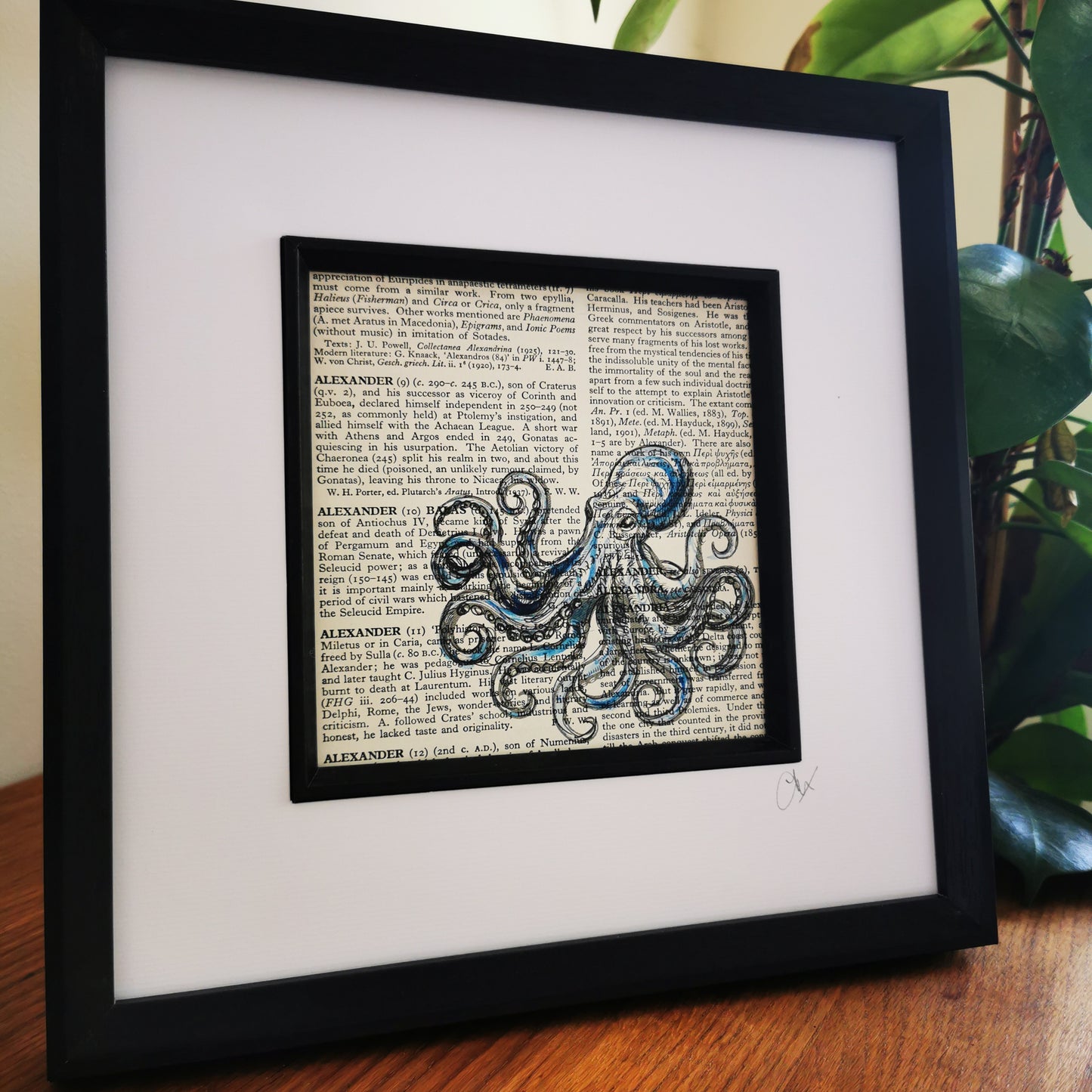 A framed and mounted artwork of a blue watercolour and ink illustration of a Kraken Octopus on a vintage dictionary page.