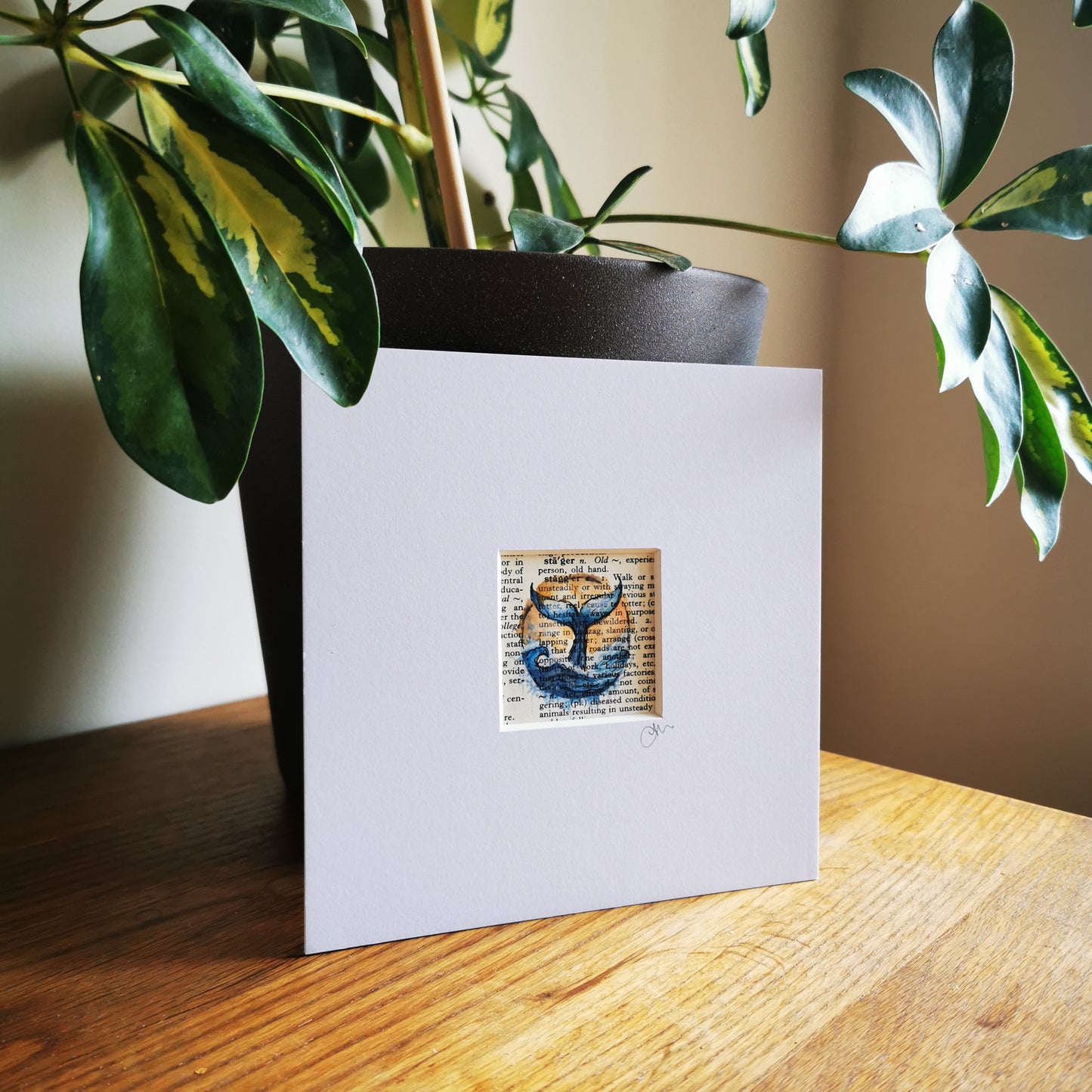 White card with a whale illustration on a wooden surface with a plant in the background