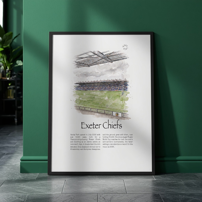 A framed vertical art print featuring a watercolour illustration of Exeter Chiefs rugby stadium and team text, leaning against a dark green wall on a dark tiled floor.