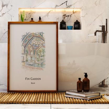 A framed art print featuring a colourful watercolor illustration of 'Fin Garden, Iran' is displayed on a bamboo mat in a modern bathroom setting next to a white bathtub.