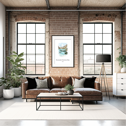 A styled living room interior with a brown leather sofa, black accent pillows, a black coffee table, brick walls, large industrial windows, potted plants, and a framed print of Huascarán National Park hanging above the sofa.