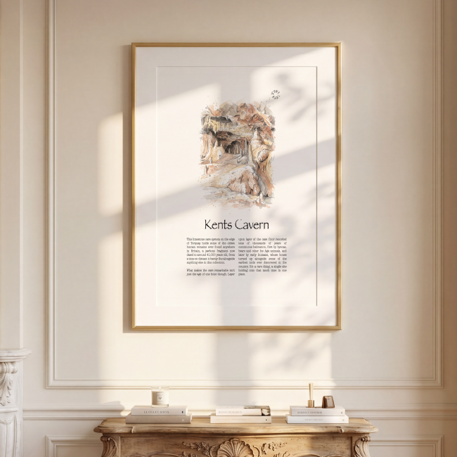 A framed art print featuring an illustration and the text 'Kents Cavern' on a cream-coloured wall in a beautifully decorated room with a gold console table, a mirror, and a window.