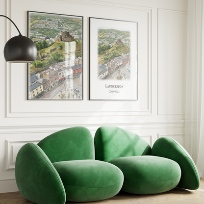 2 art prints of Launceston castle and Town Centre seen from above, displayed on a white wall with quirky green sofa in front and arched floor light.
