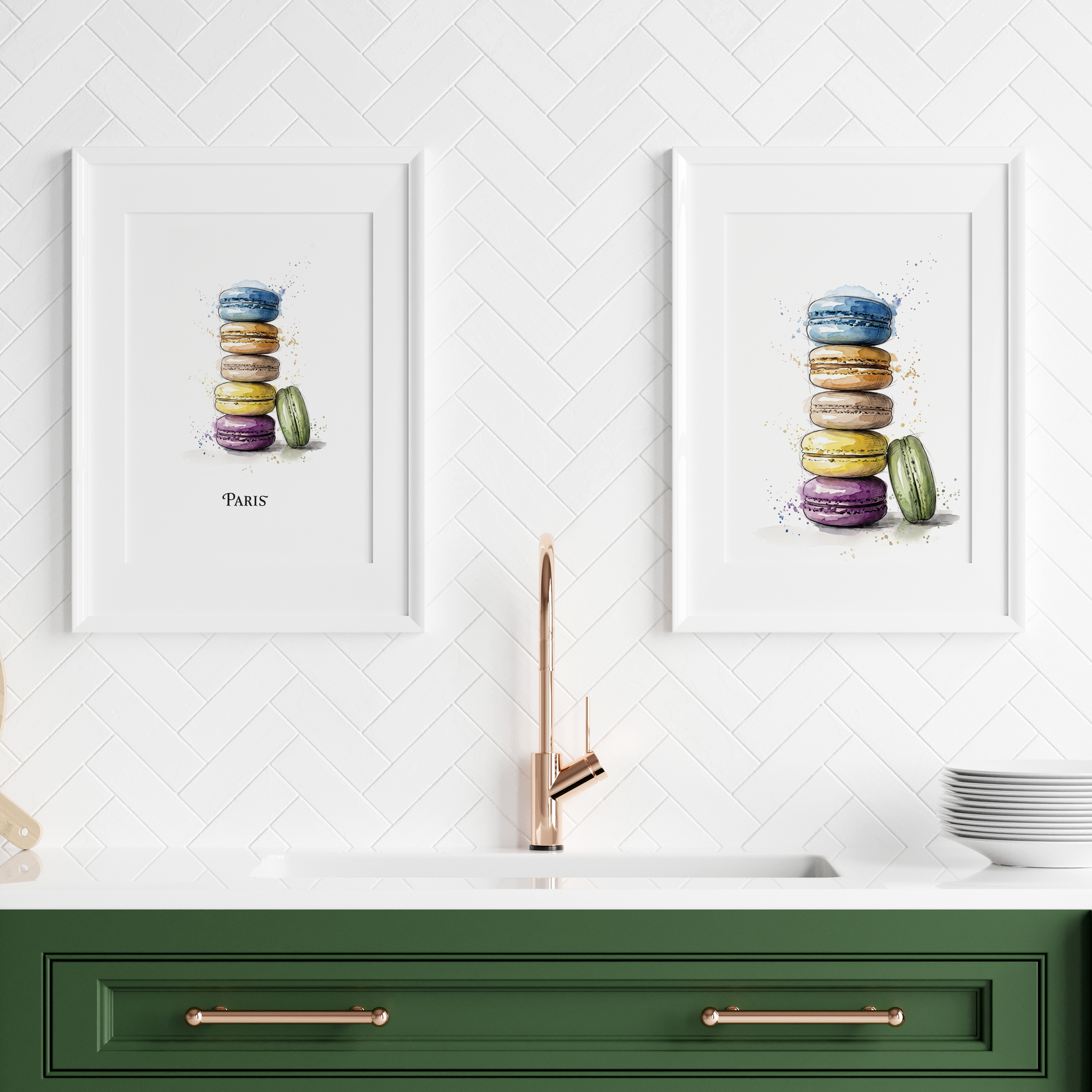 Two framed watercolour prints of stacked macarons hang on a white herringbone wall above a green kitchen counter with a faucet, plates, and a wooden board.
