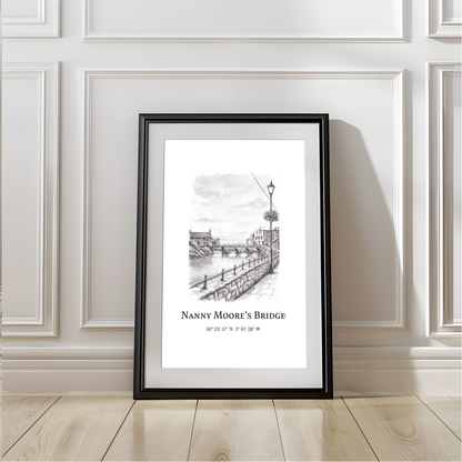 A framed black and white architectural sketch print of 'Nanny Moore's Bridge' leaning against a white paneled wall on a light wood floor.