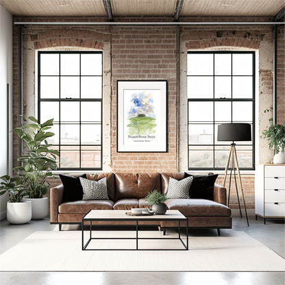 A styled living room featuring a brown leather sofa with black and white patterned pillows, a black metal coffee table, a white rug, brick walls, and two large industrial windows. A framed art watercolour print  of The Nearly Home Trees on the Devon/Cornwall border hangs on the wall above the sofa.