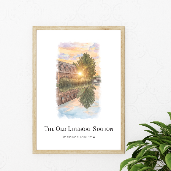 A framed art print featuring a watercolour illustration of 'The Old Lifeboat Station' with coordinates below, displayed on a light patterned wall next to a green plant.