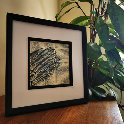 original watercolour and ink painting on a vintage book page in a black frame on a wooden desk, with a plant behind