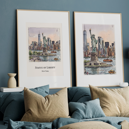Two framed watercolour art prints of the Statue of Liberty and New York City skyline against a dark blue wall on a shelf above a bed with blue and beige pillows, a wooden lamp, and books.