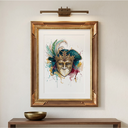 Framed wall art featuring a colourful watercolour-style masquerade mask, displayed on a beige wall above a wooden console table with a small bowl. A wall-mounted light fixture is visible above the frame.