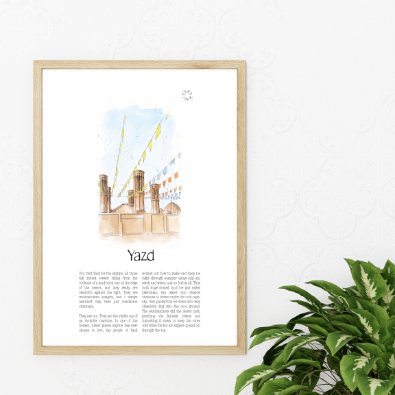 A framed art print featuring a watercolour illustration of the Yazd cityscape with text below, displayed on a white wall next to a green potted plant.