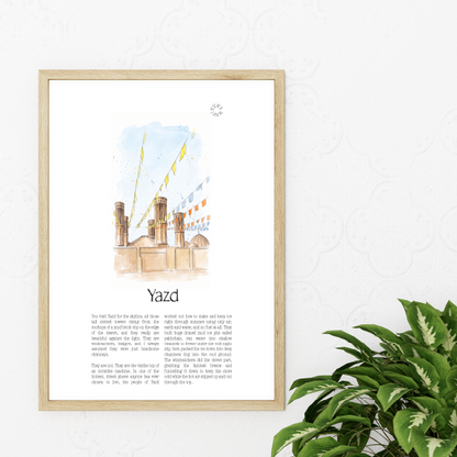A framed art print featuring a watercolour illustration of the Yazd cityscape with text below, displayed on a white wall next to a green potted plant.