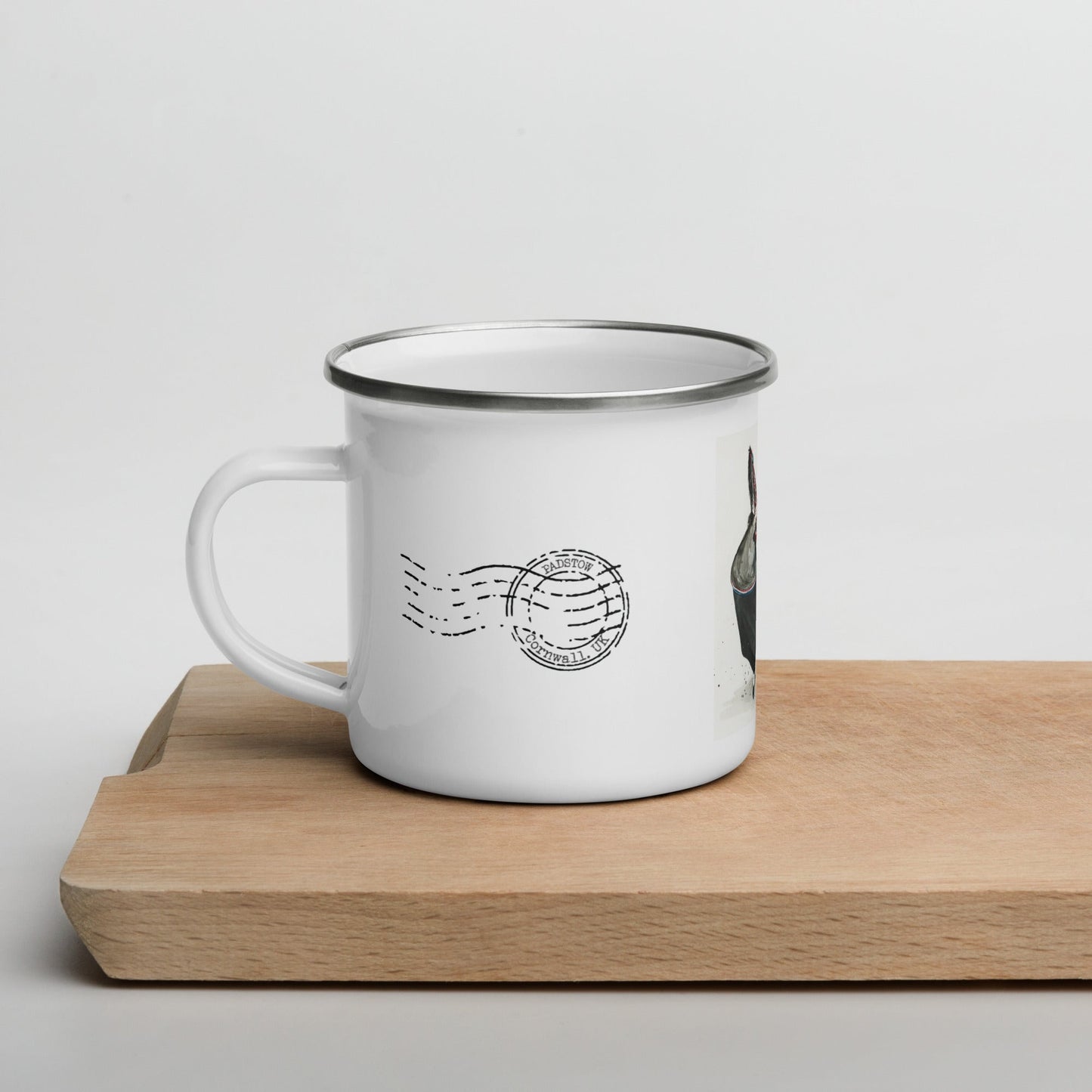 White enamel mug with black padstow postmark, with the cup on a wooden chopping block surface