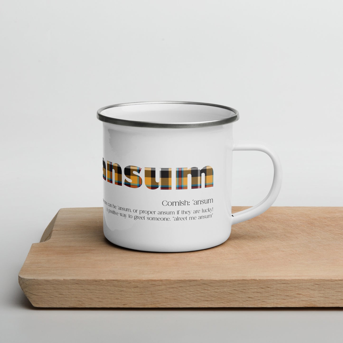 white enamel mug with cornish tartan text saying ansum on a wooden chopping board