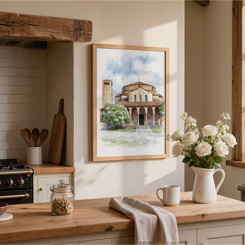 A framed watercolor painting of Torcello Church Venice, hangs on a beige wall in a beautifully styled, sunlit kitchen with wooden countertops, white flowers in a pitcher, and a window.